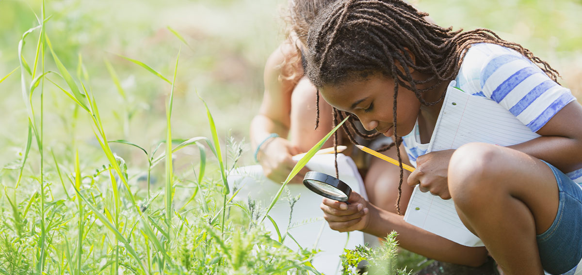 pre-teen outdoors using a magnifying glass to examine nature